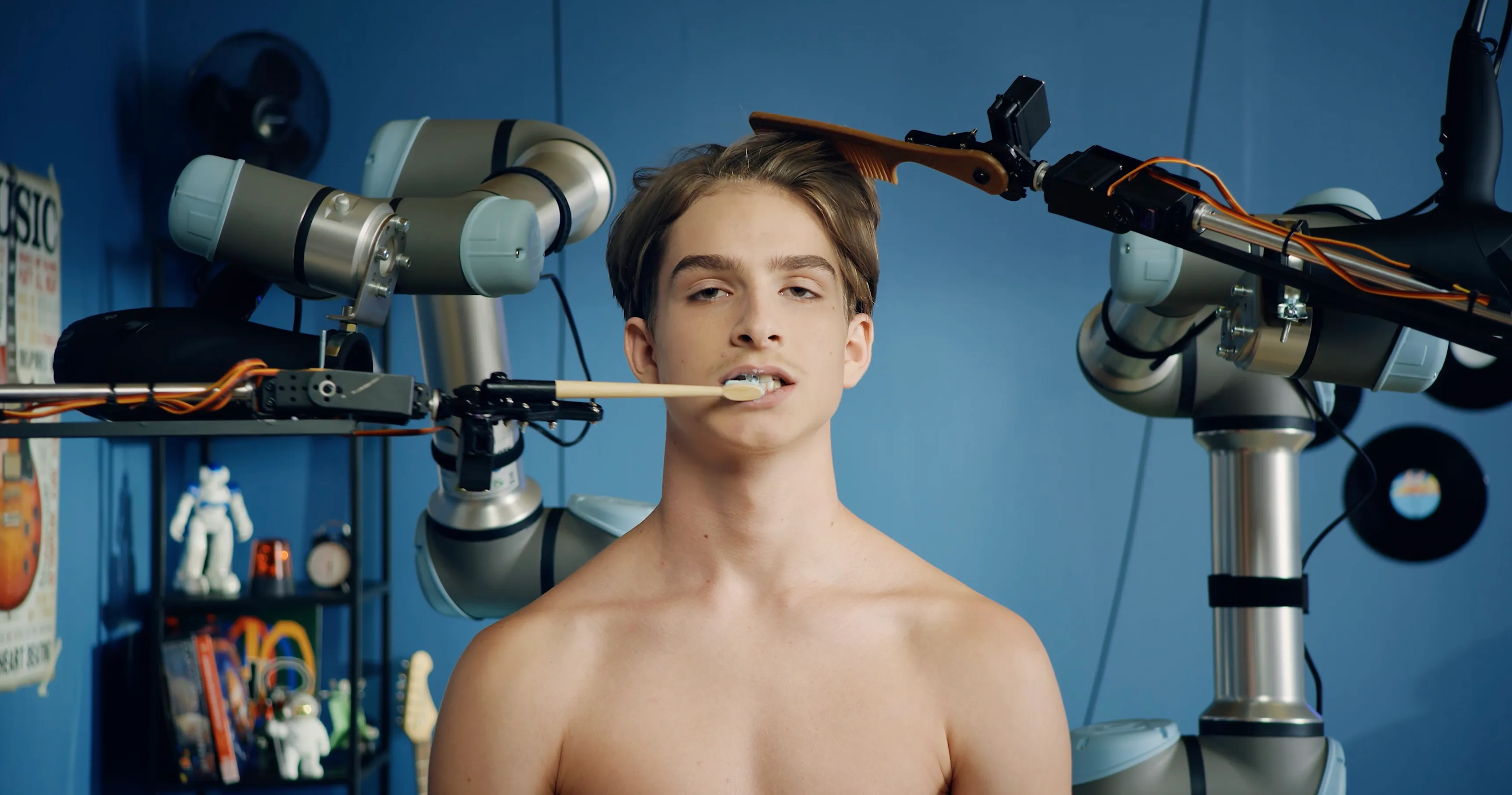 Ein junger Mann lässt sich von einem Roboterarm die Zähne putzen, ein zweiter Roboterarm kämmt ihm die Haare
